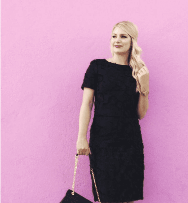 Emily Williams wearing a black dress standing against a pink wall
