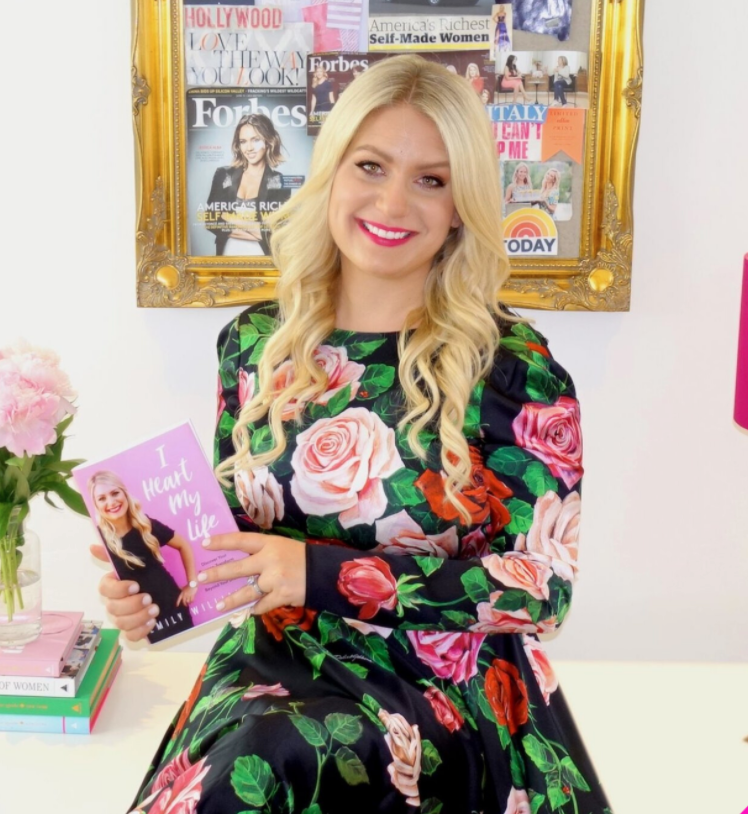 Emily Williams in a floral dress holding the I Heart My Life book