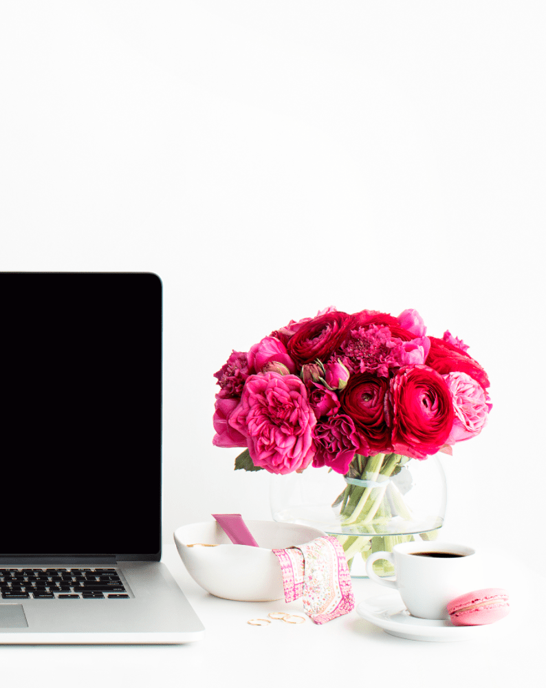 Laptop on desk with pink flowers beside it