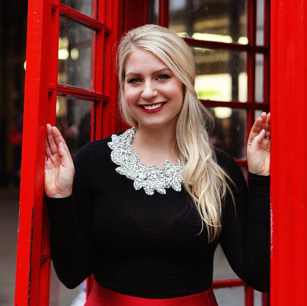 Emily Williams standing inside a red telephone booth in London