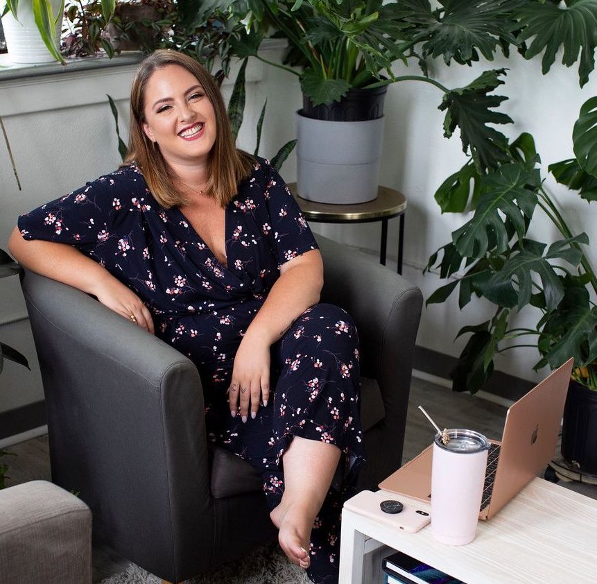 Jennifer Spivak in a black floral dress sitting on a black chair with a rose gold laptop