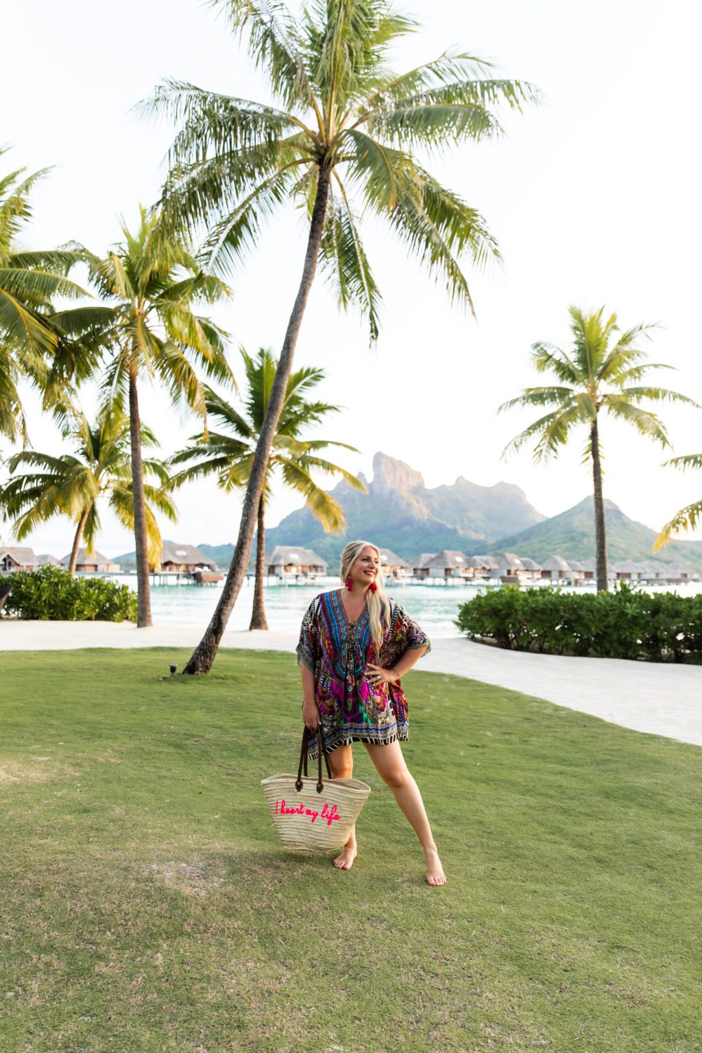 Emily on a lawn in Bora Bora with palm trees and overwater bungalows behind her