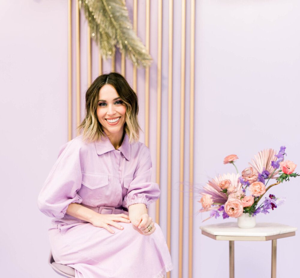 Jaclyn Johnson in Lilac dress and flooring with pink and lavender flowers on top of the table